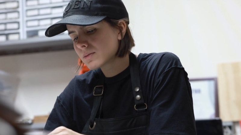 Žena u radnoj kecelji i kačketu radi u maloj proizvodnoj radionici