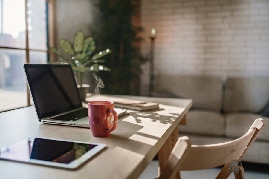 Laptop i šolja kafe na radnom stolu u kućnoj kancelariji pored prozora, sa prirodnim svetlom i modernim minimalističkim enterijerom.