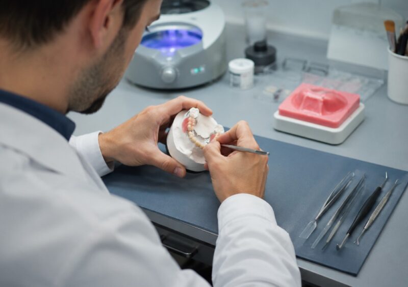 Stomatološki tehničar izrađuje zubnu protezu na radnom stolu u stomatološkoj laboratoriji